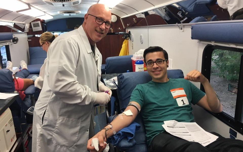 Male donor and male phlebotomist smiling during blood donation on mobile bus
