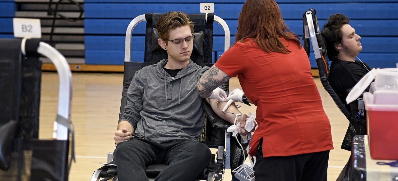 Young male donor giving whole blood at a high school blood drive.