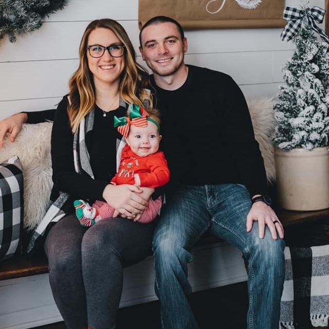 Kendra Stanley and her husband sitting with baby Addison in a Christmas outfit